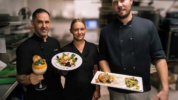 Trois personnes, chacune tenant une assiette de nourriture, dans une cuisine.