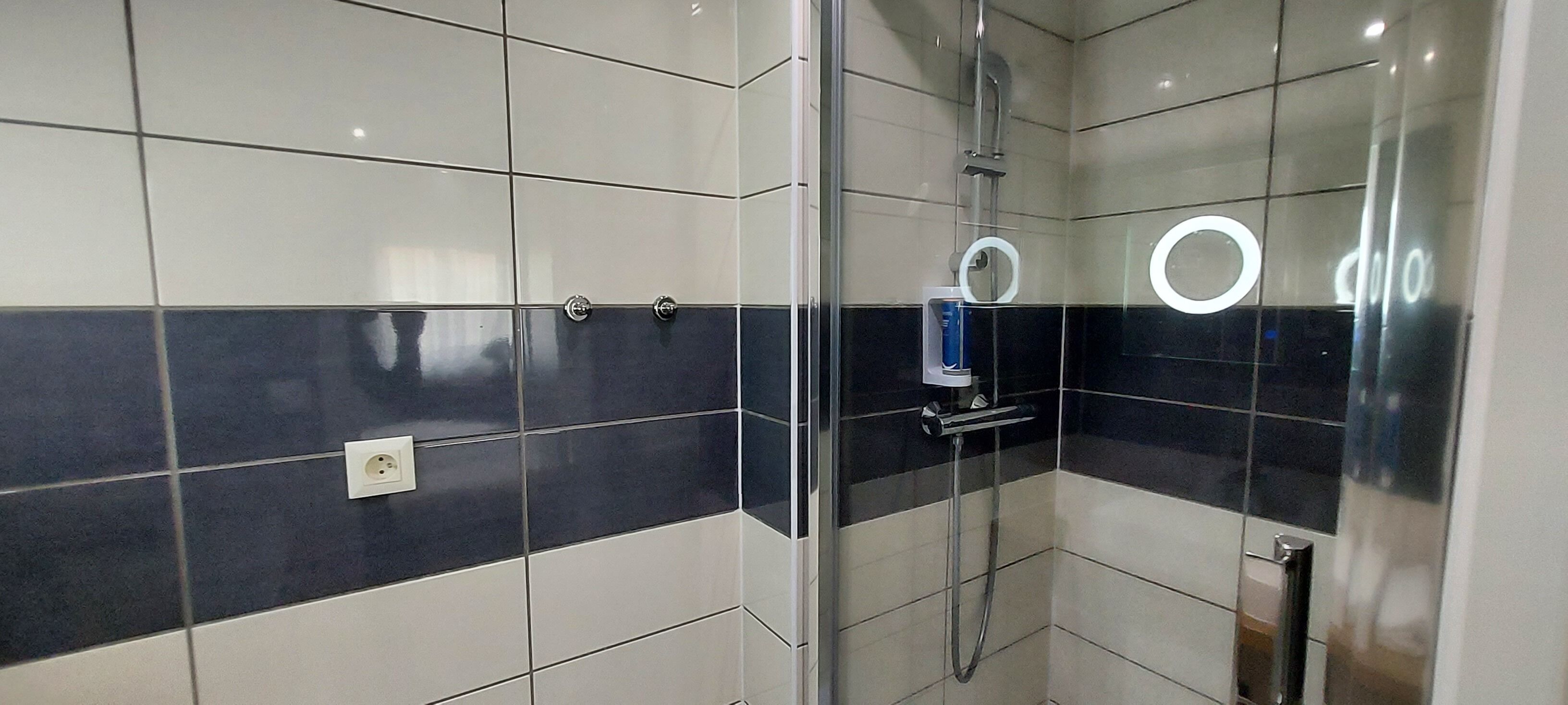 Casa de banho moderna com cabine de duche em vidro, chuveiro manual e espelho de mão.