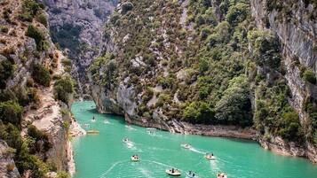 A canyon with boats on a turquoise river surrounded by rocky cliffs and greenery.