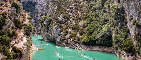 A canyon with boats on a turquoise river surrounded by rocky cliffs and greenery.