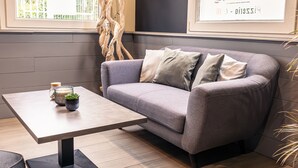 A modern living room with a grey sofa, a wooden coffee table, and a small potted plant. - Brit Hotel Confort Manosque Cadarache (Manosque)