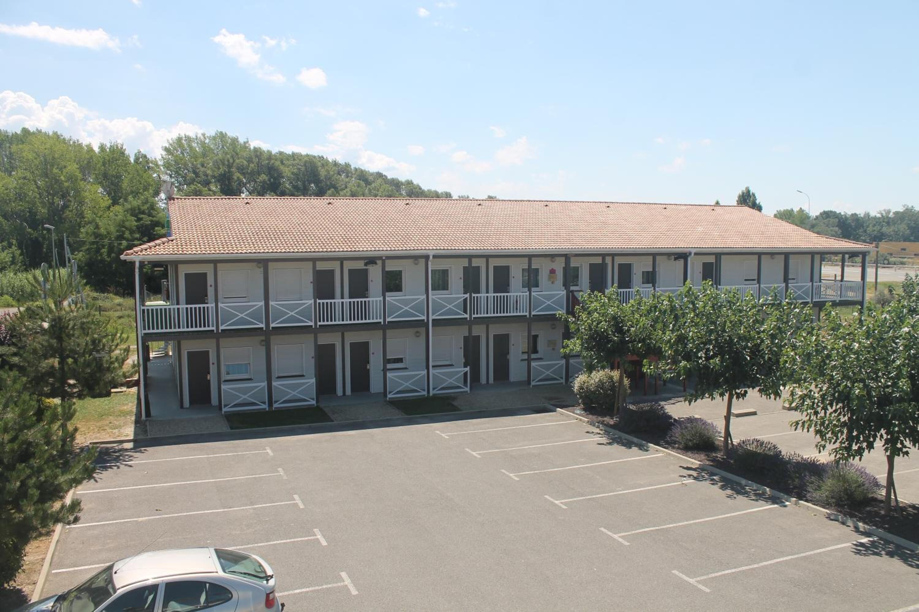 A two-story motel with a tiled roof, multiple balconies, and a parking lot.
