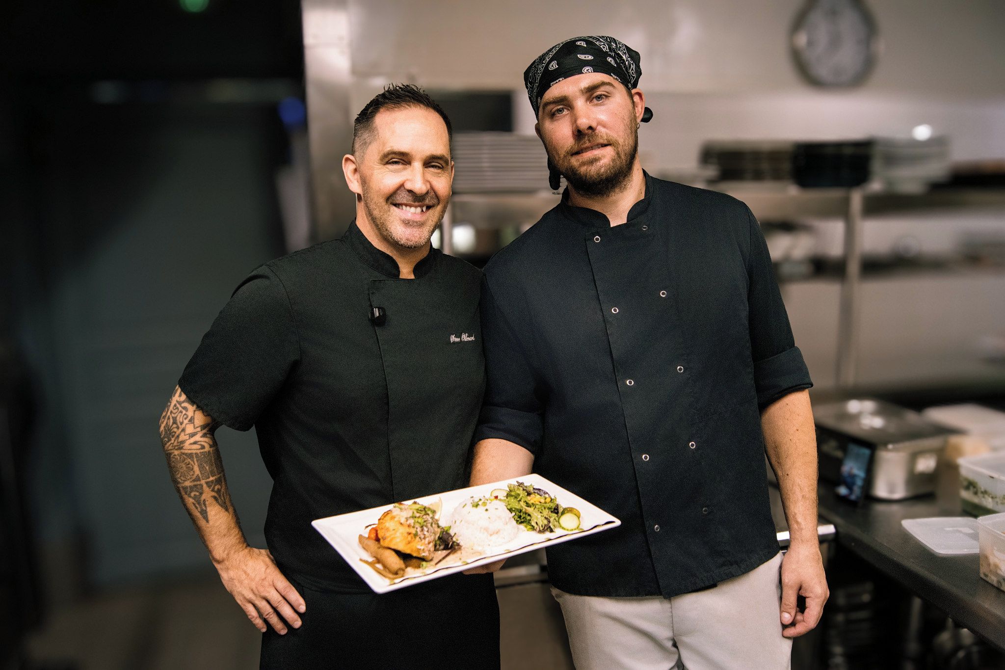 Deux chefs, dans une cuisine, tenant une assiette de nourriture.