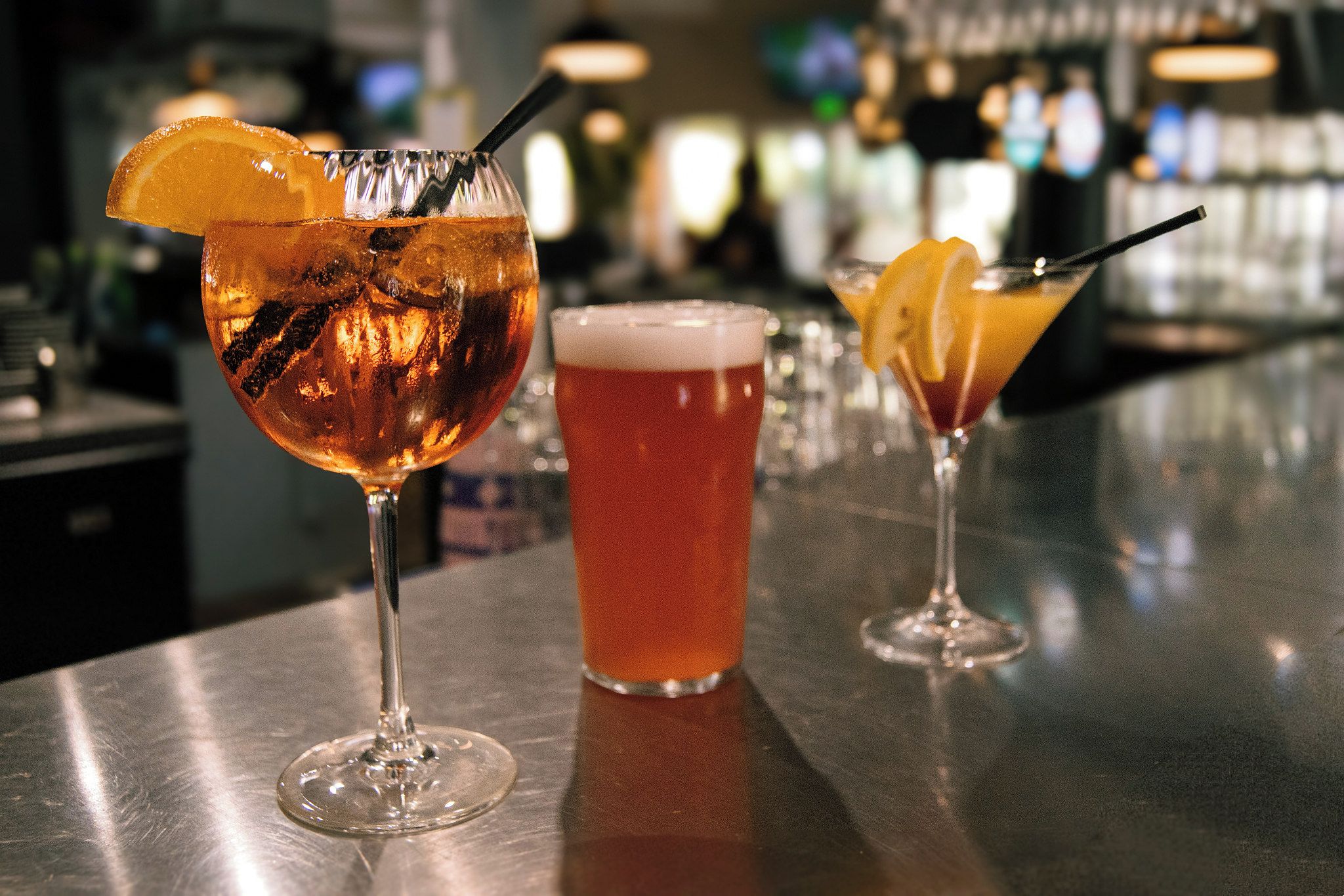 Three glasses of beverages on a bar counter.