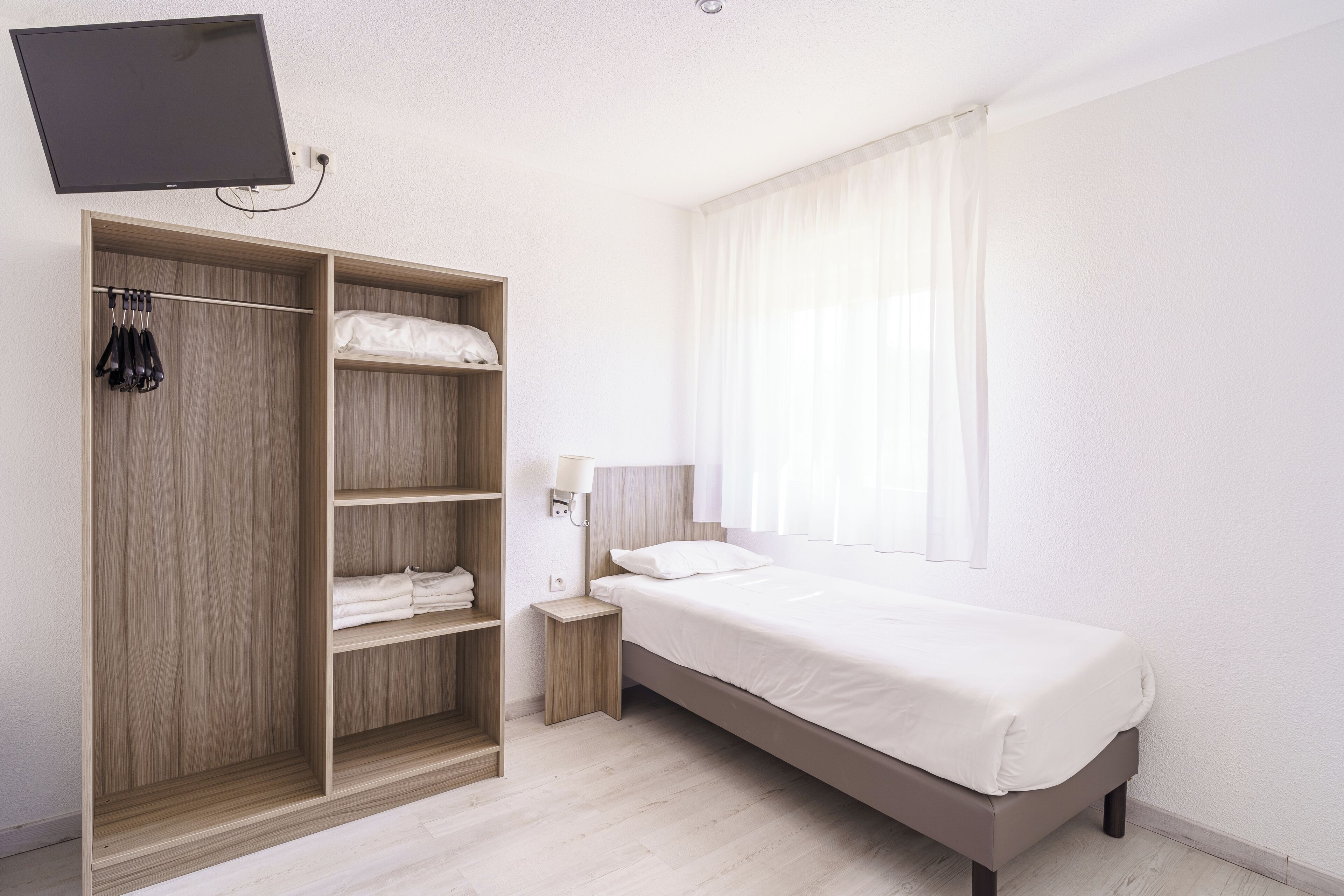 A modern bedroom with a bed, a wardrobe, a bedside table, a lamp, and a TV mounted on the wall.