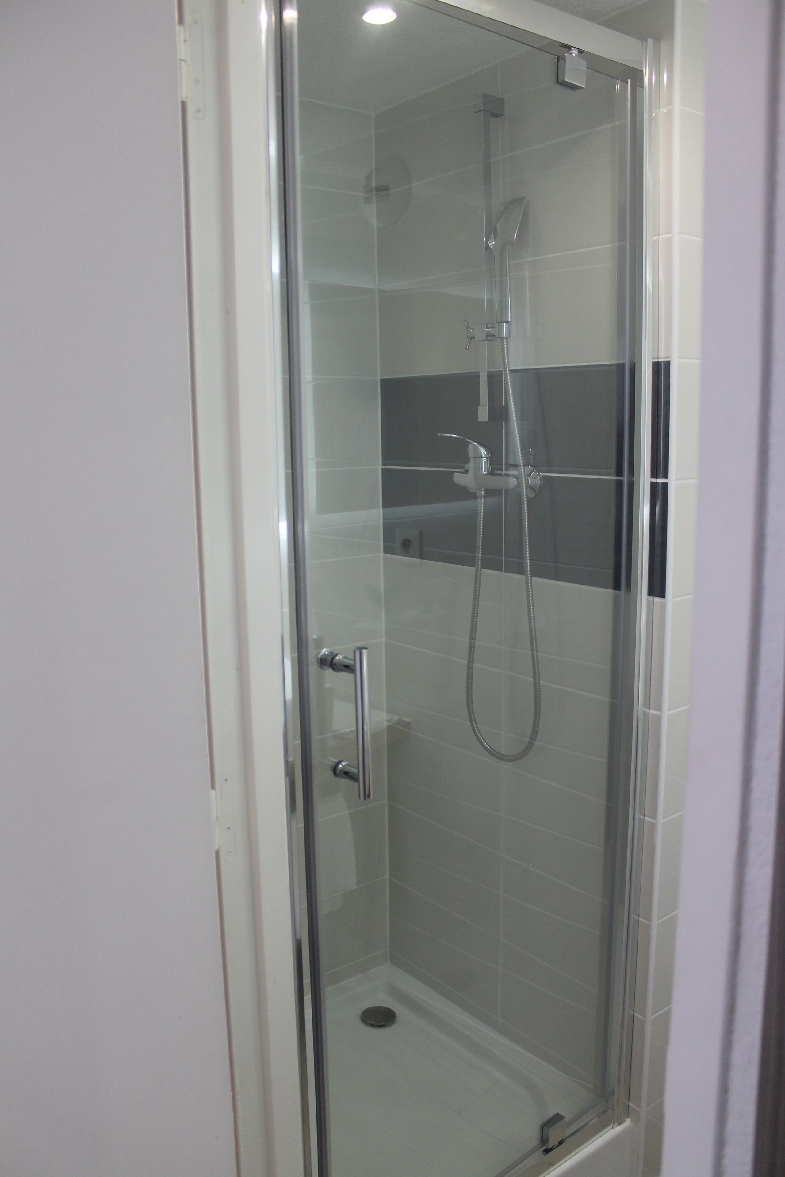Une cabine de douche fermée par des parois en verre, dotée d’un pommeau de douche à main et d’un robinet fixé au mur.
