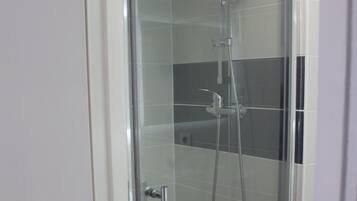 Une cabine de douche fermée par des parois en verre, dotée d’un pommeau de douche à main et d’un robinet fixé au mur.