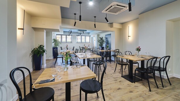 A modern dining area with multiple tables and chairs, ceiling lights, and a visible air conditioning unit. - Hotel Halo Toruń (Torun)