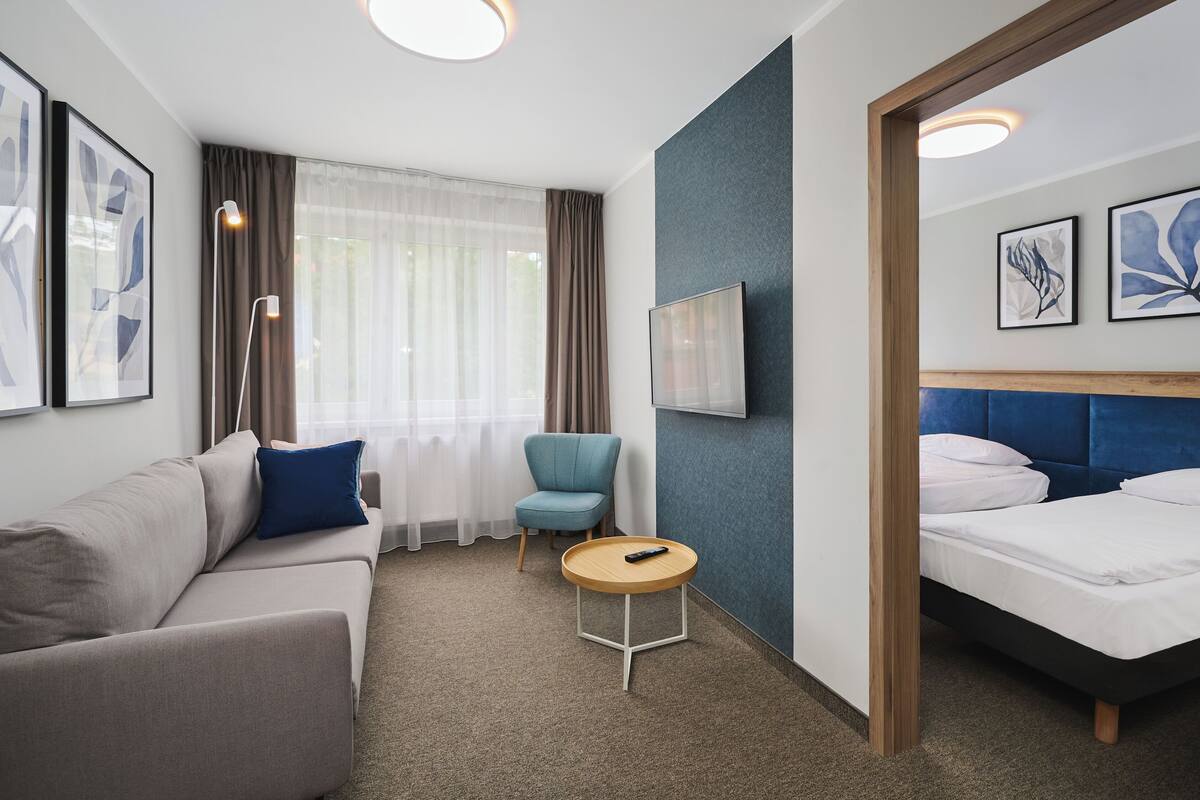 Ein Hotelzimmer mit Bett, einer Couch, einem Sessel, einem kleinen Tisch und einem Fernseher.