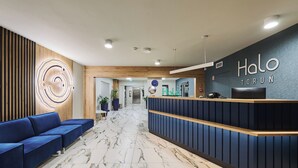 A hotel reception area with a modern design, featuring a reception desk, a blue seating area, and a marble floor. - Hotel Halo Toruń (Torun)