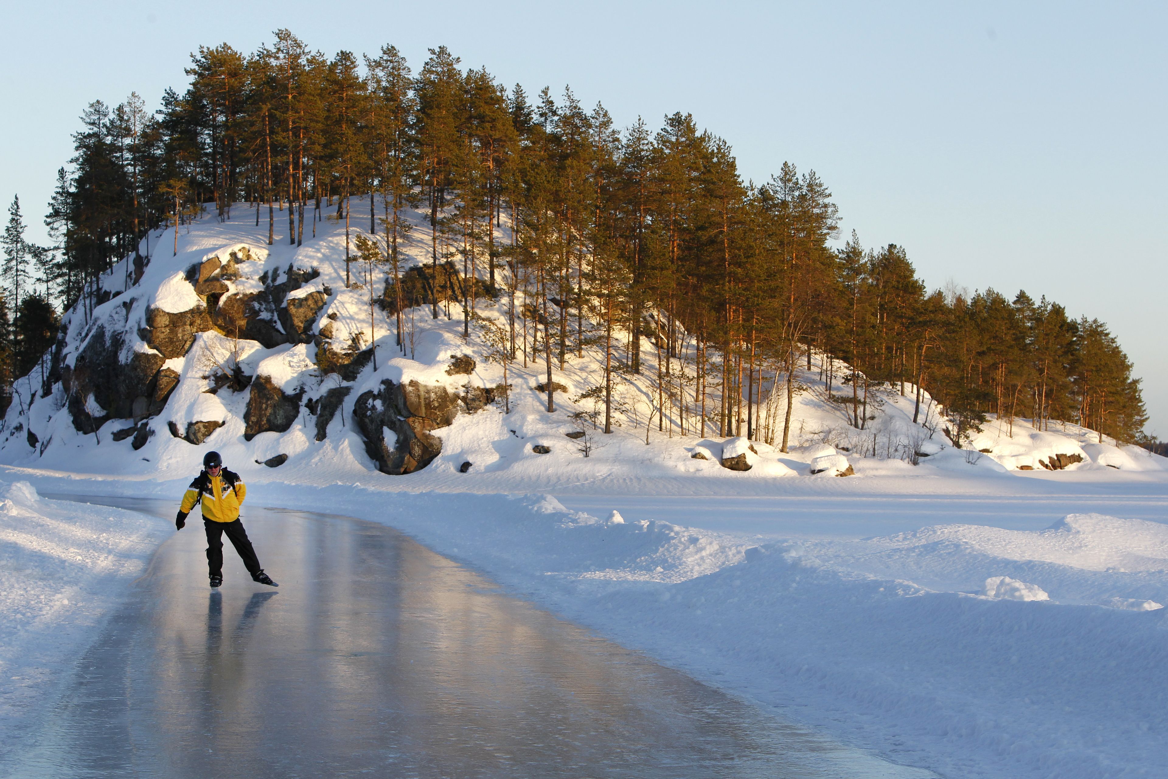 Iemand schaatst over een bevroren meer, met besneeuwde rotsen en bomen op de achtergrond.