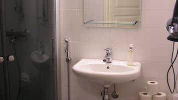 A bathroom with a glass-enclosed shower, a sink with a mirror above it, and a wooden shelf with towels.
