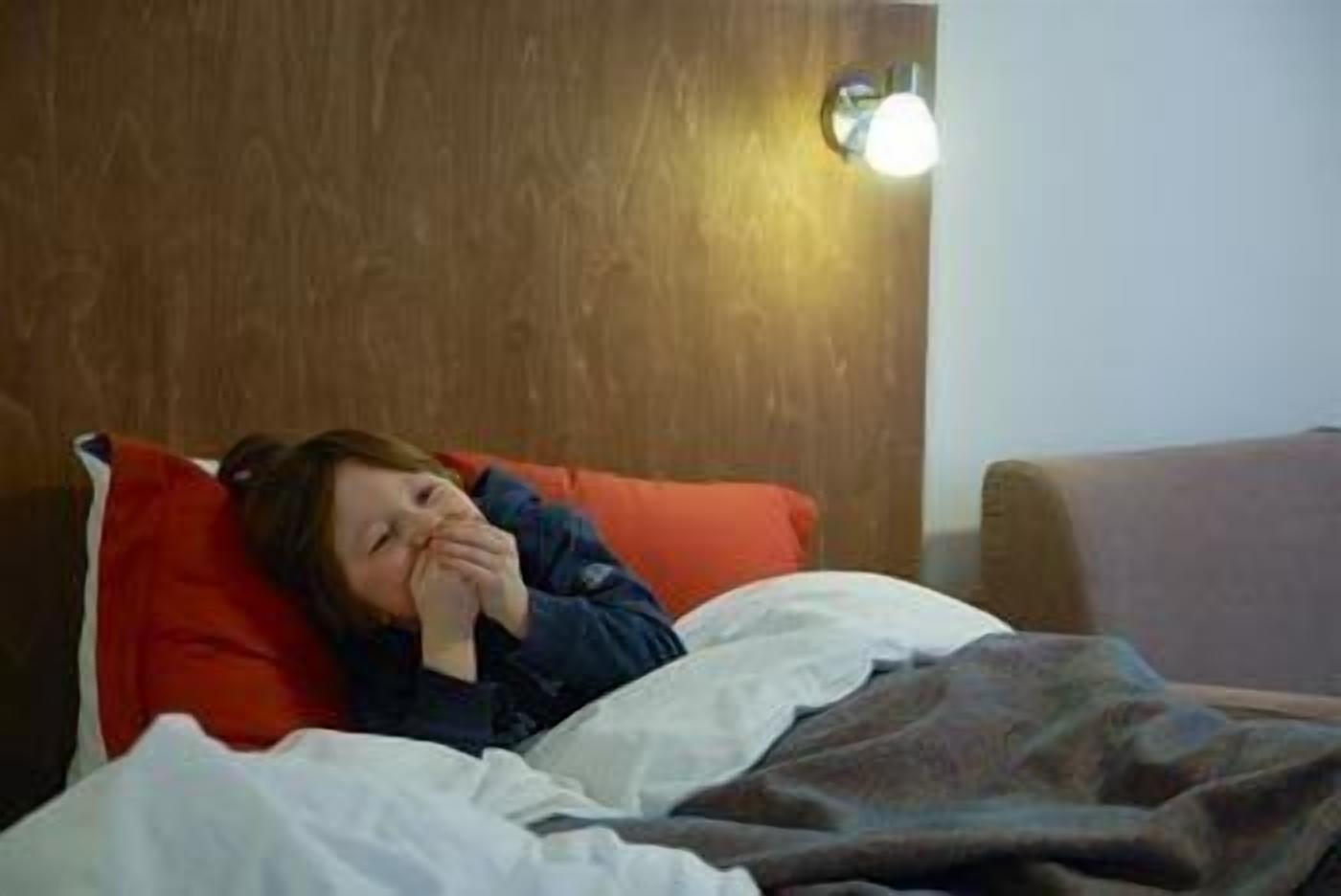 Una persona acostada en una cama con una almohada roja y sábanas blancas.