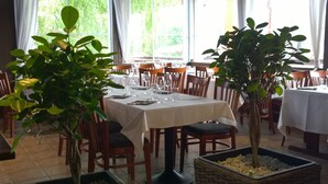Restaurante com mesas preparadas para refeições, rodeado por cadeiras e plantas em vasos.