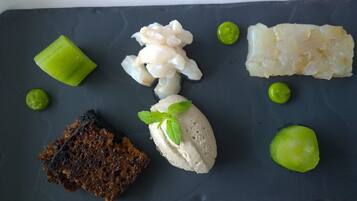 A dark slate serving board with various food items including a piece of dark bread, a scoop of ice cream garnished with mint leaves, and several pieces of white fish.