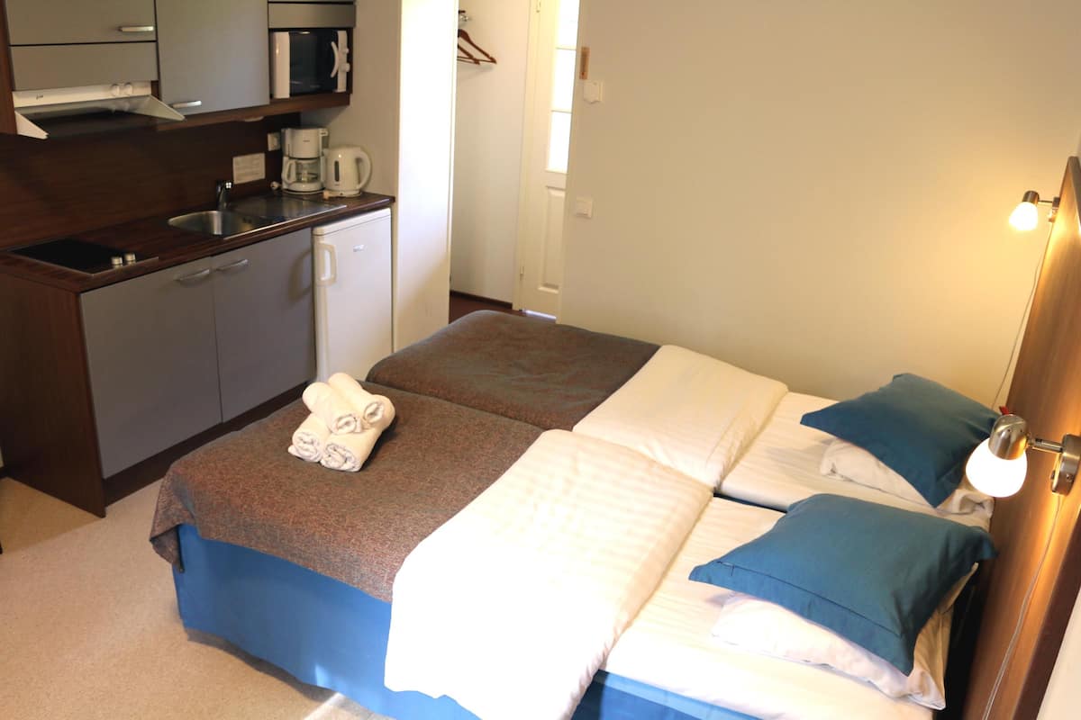 Ein Hotelzimmer mit Küchenzeile, zwei Betten mit blau-weißer Bettwäsche und einer Nachttischlampe.