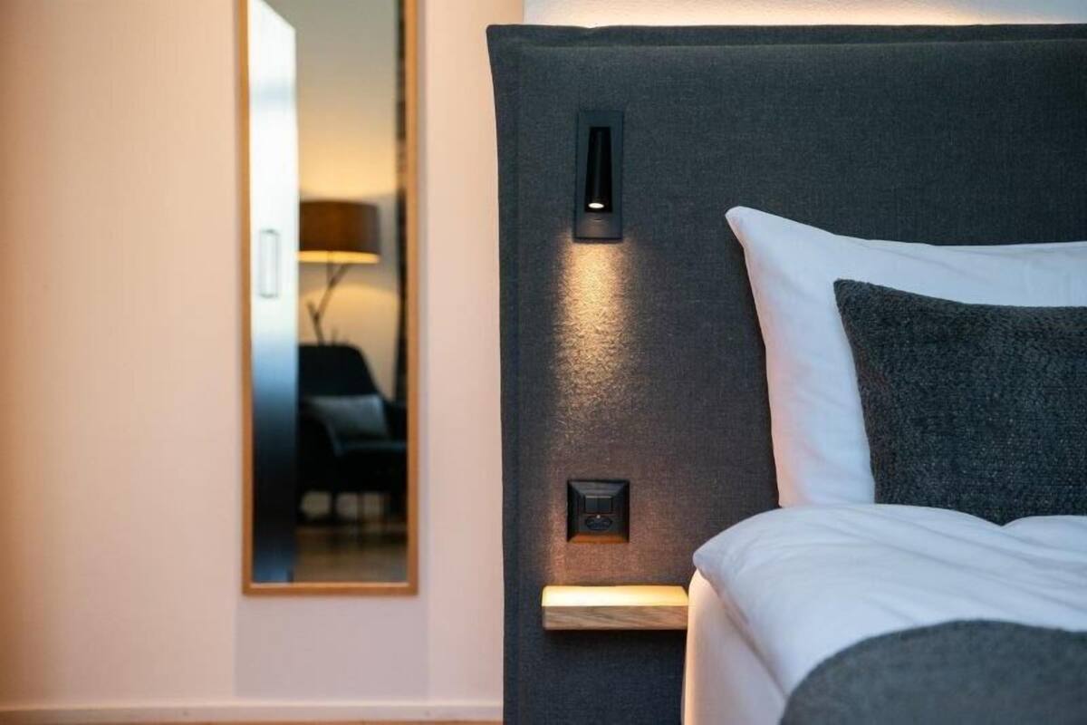 A hotel room with a large bed, a nightstand, and a wall-mounted control panel.