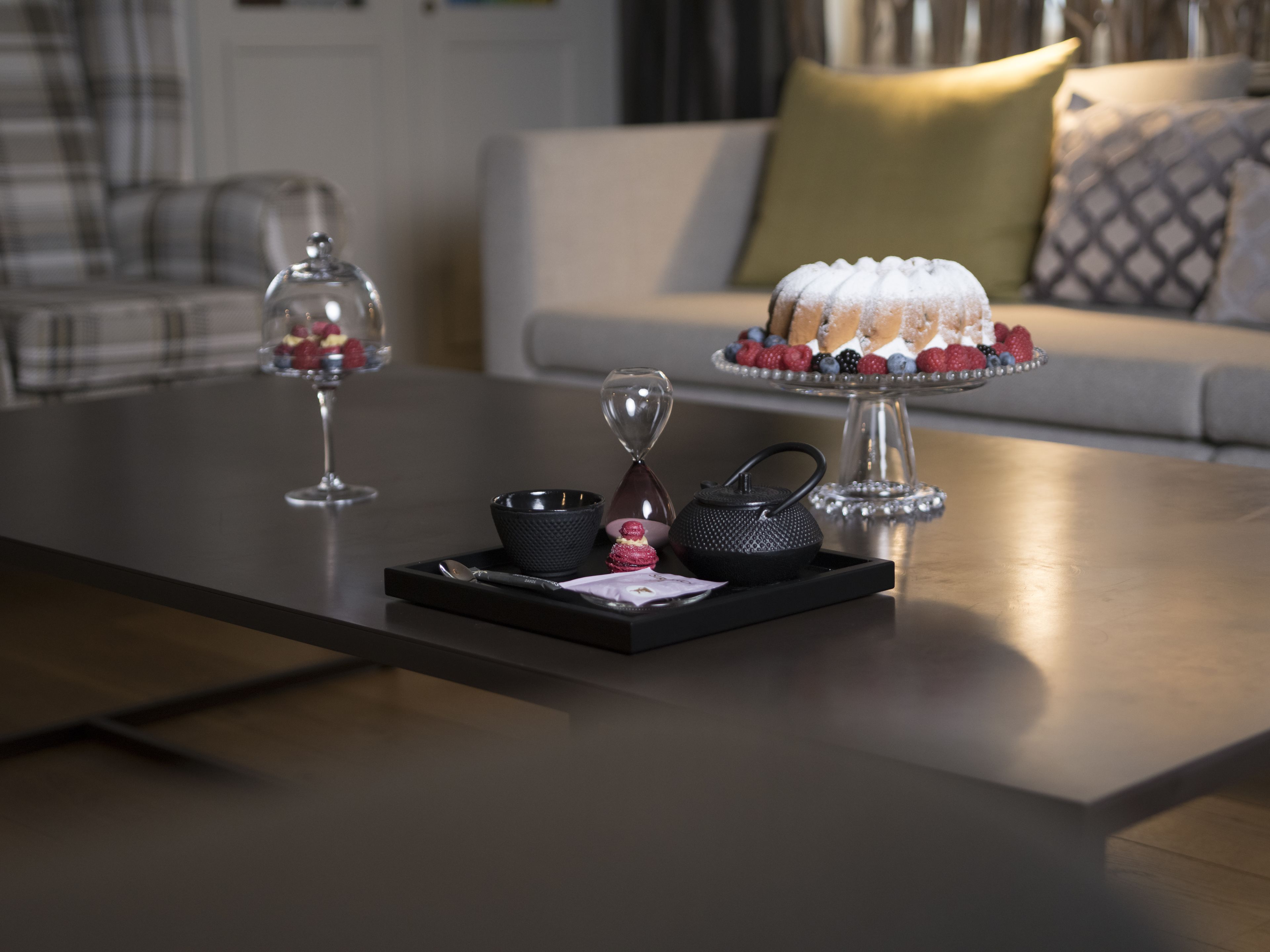 Une table à manger avec un plateau de desserts, une théière et un verre.