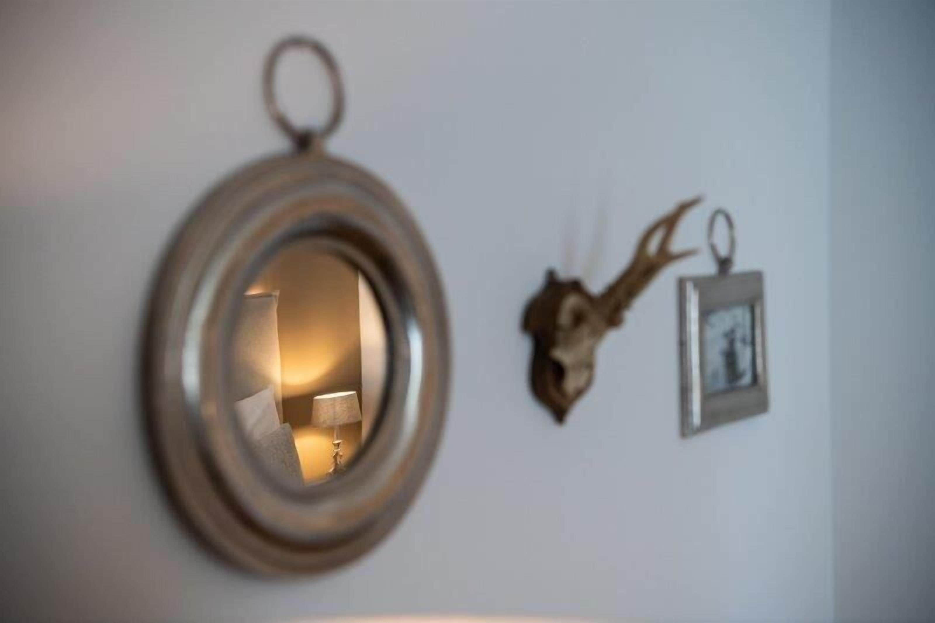 Uno specchio rotondo con una lampada integrata, fissato a una parete accanto a un portafoto.