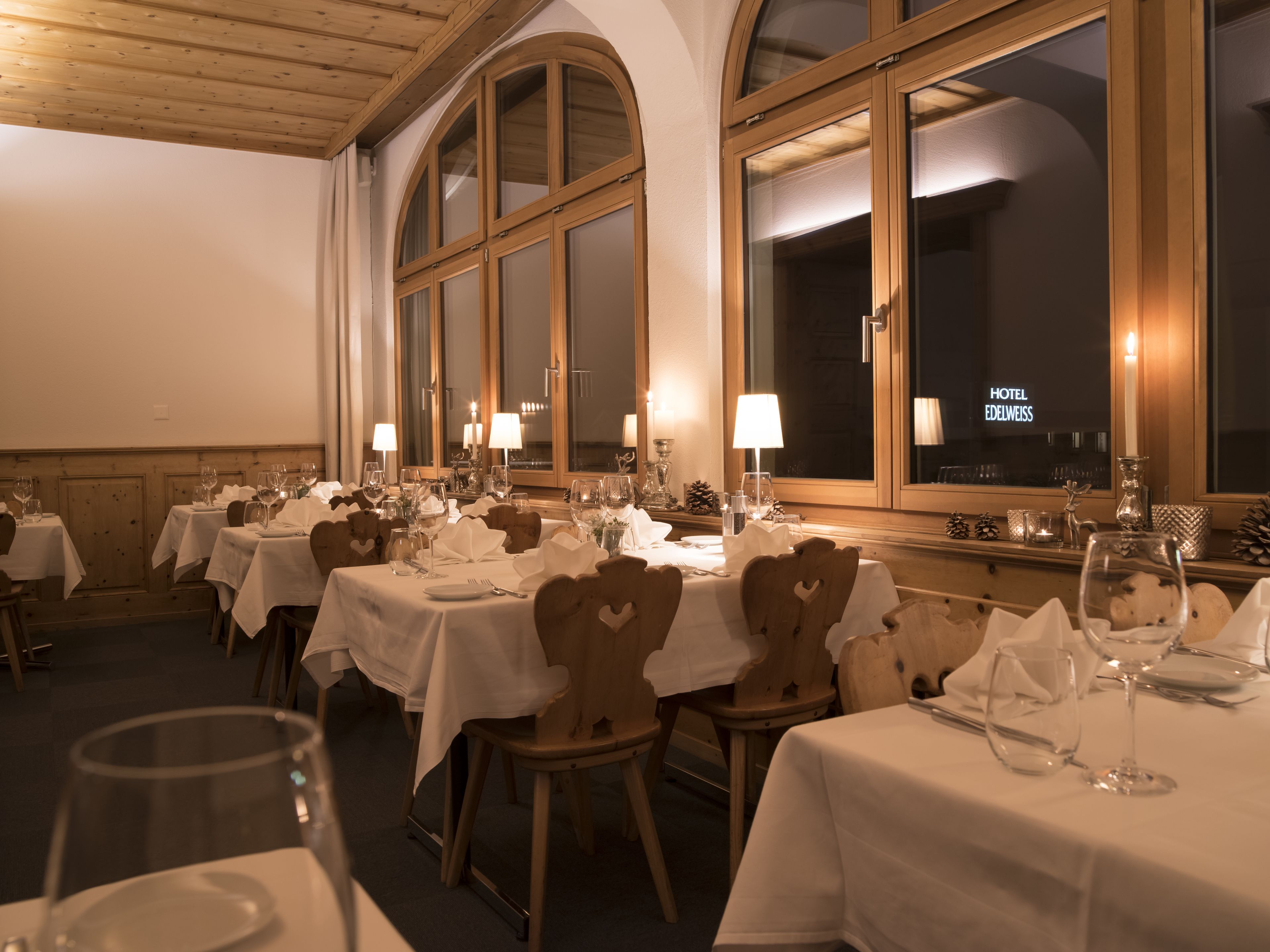 Un restaurante con varias mesas dispuestas para comer, cada una con mantel blanco y velas.