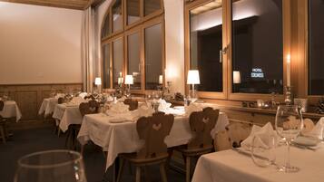 Un restaurante con varias mesas dispuestas para comer, cada una con mantel blanco y velas.