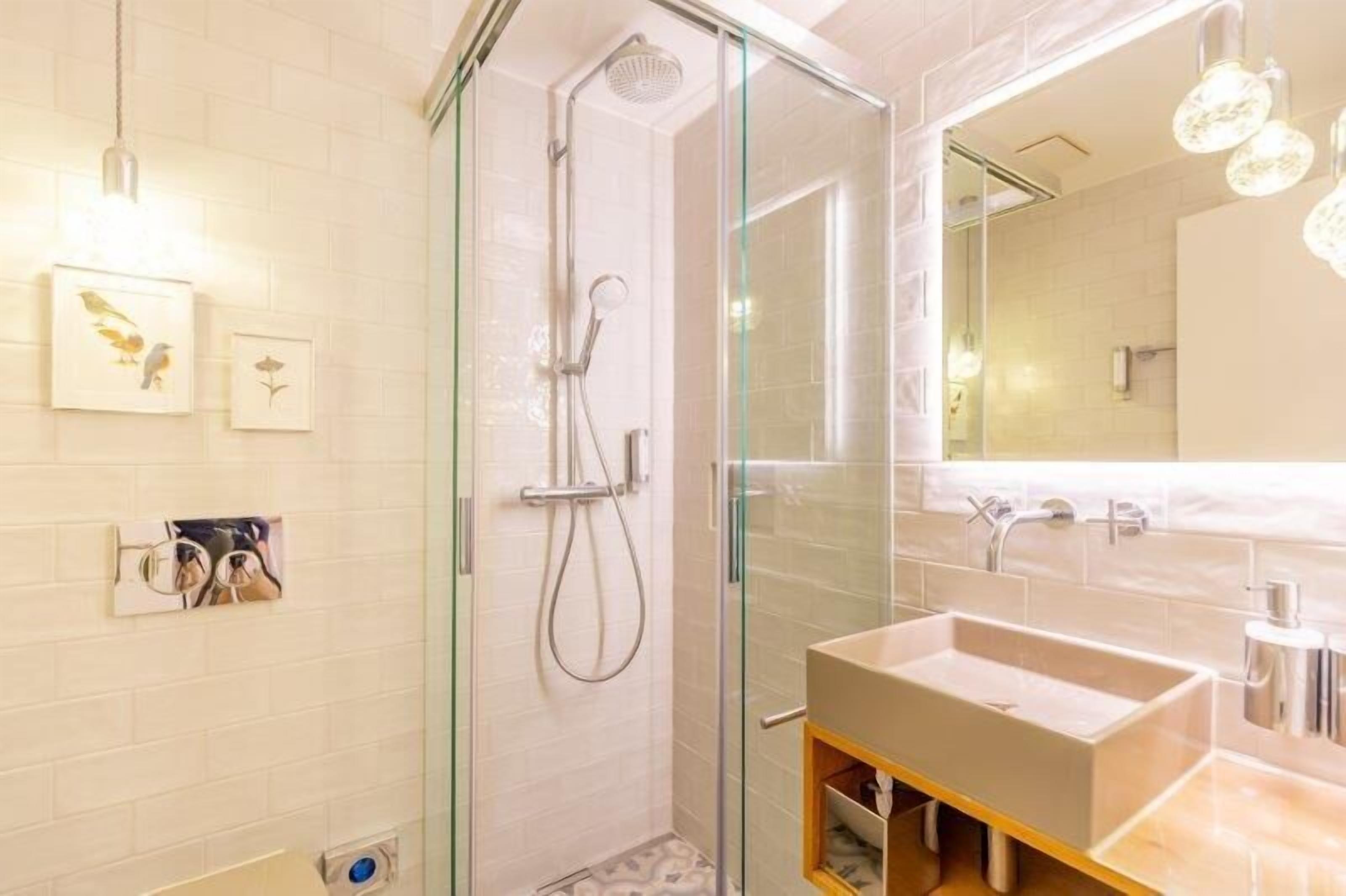 Un baño moderno con ducha envuelta en vidrio, un espejo grande y un lavabo rectangular.