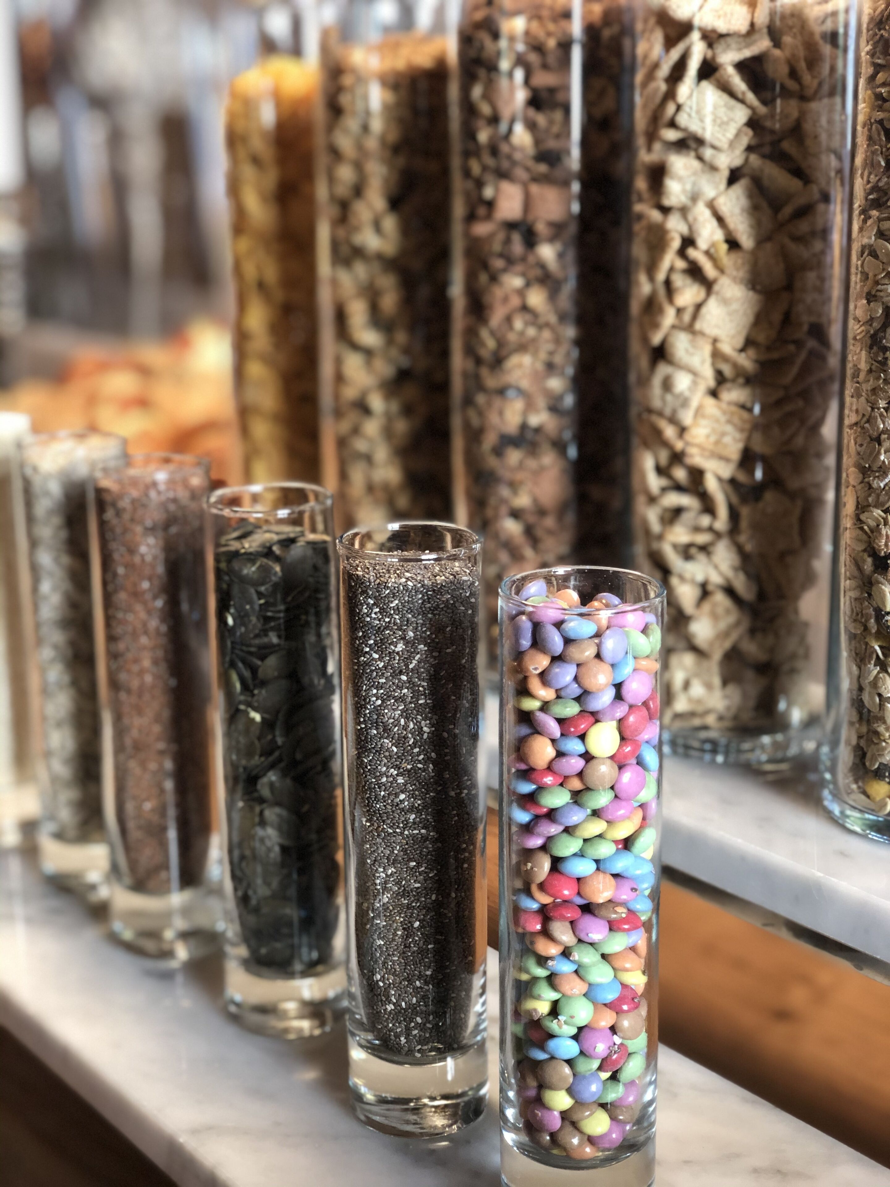 A row of glass containers filled with various materials like seeds, grains, and colorful beads.