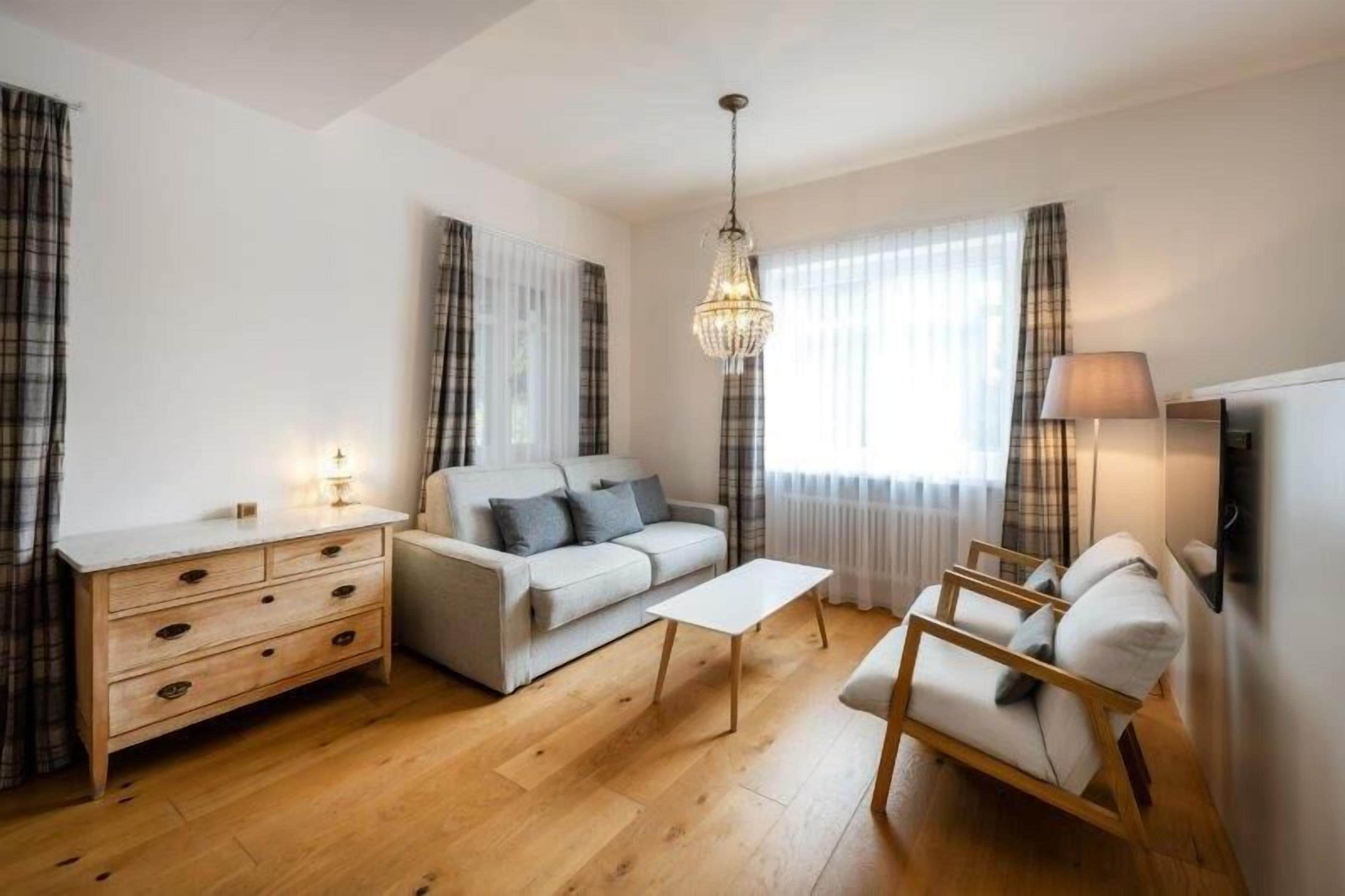 Una sala de estar moderna con un sofá, una mesa de centro, una mesita de noche de madera, un sillón y una araña.
