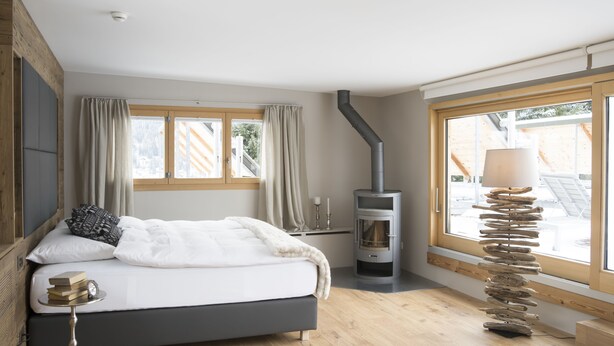 Une chambre à coucher avec un lit, un plancher en bois, une fenêtre avec des rideaux, une cheminée et une lampe.