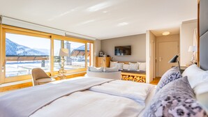A hotel room with a large bed, a chair, a desk, and a TV. There is a window with a view of mountains. - Hotel Edelweiss (Davos)
