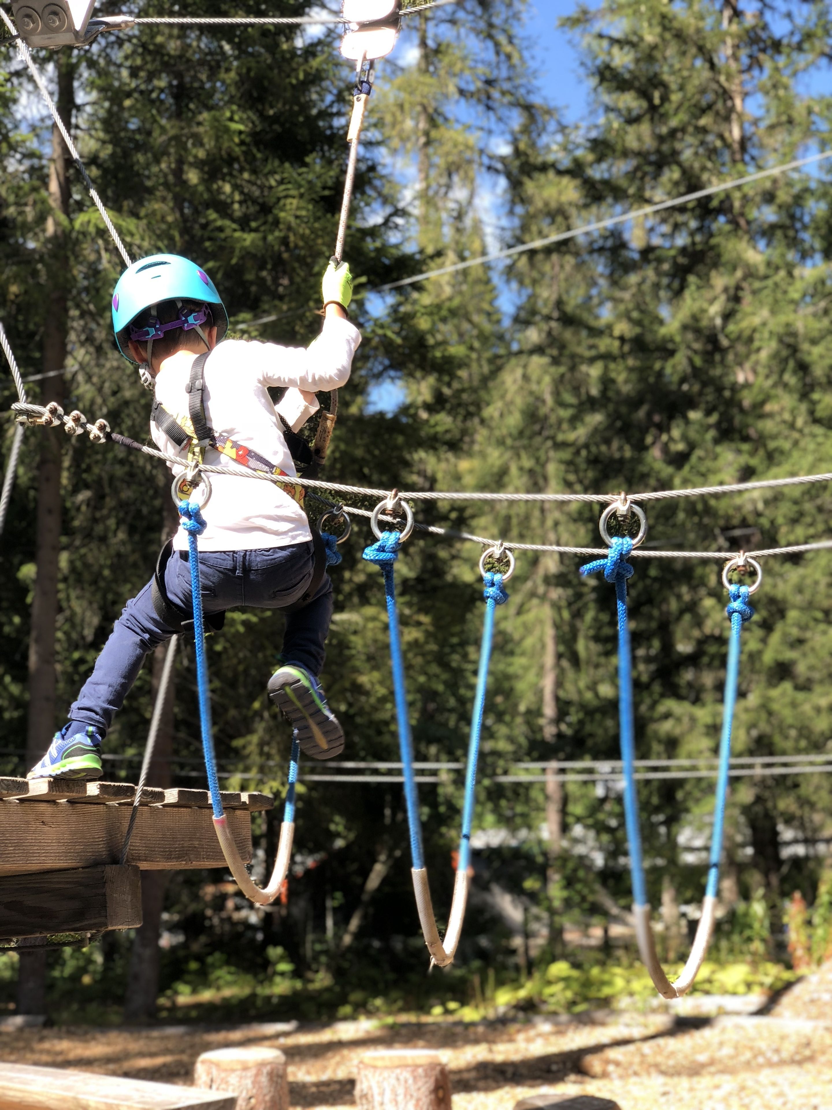 Une personne qui se déplace sur un parcours d’obstacles en plein air, composé de cordes et de plateformes en bois.