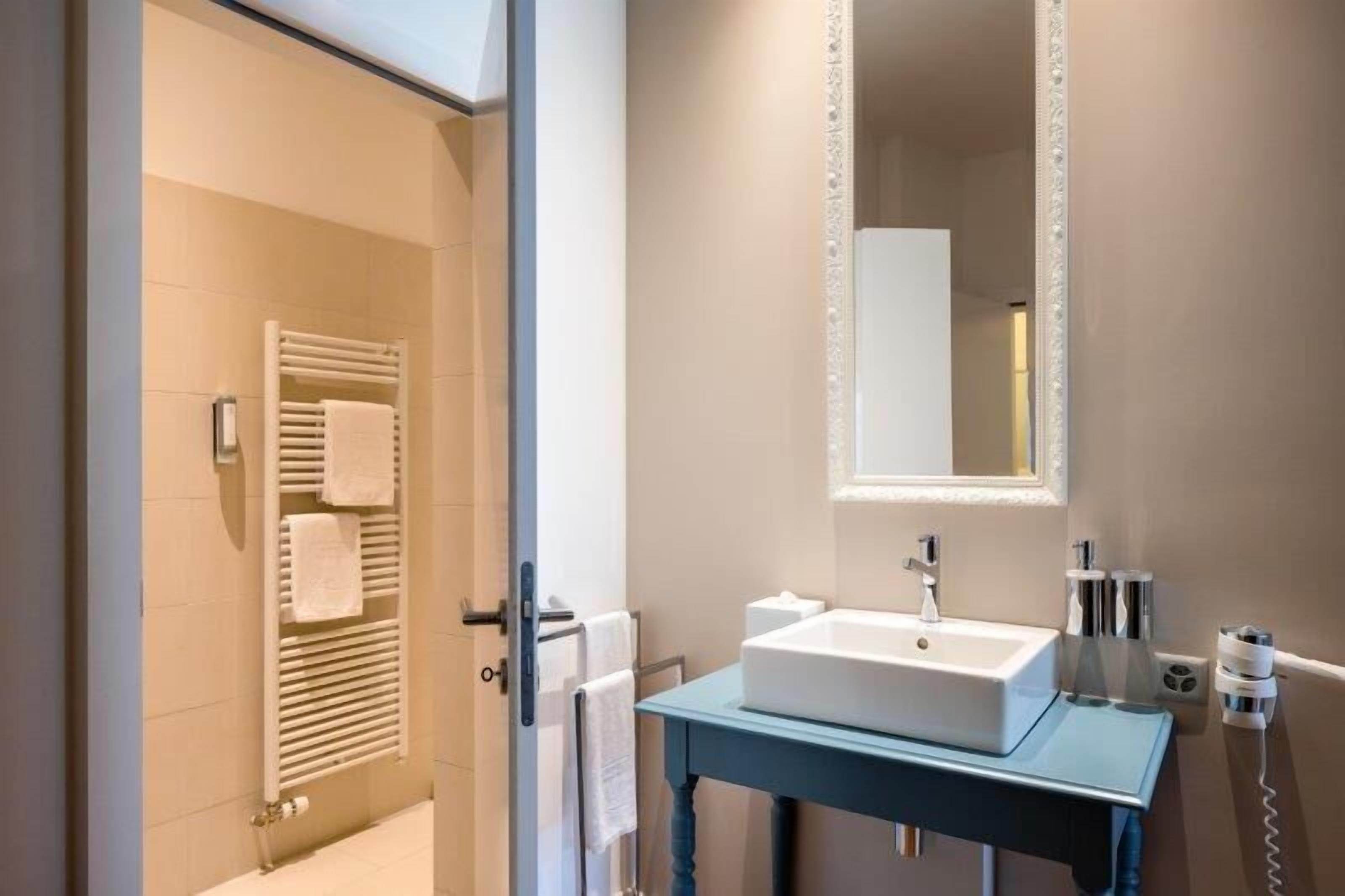 Un baño con lavabo, espejo, toallero y una puerta que da a la zona de ducha.