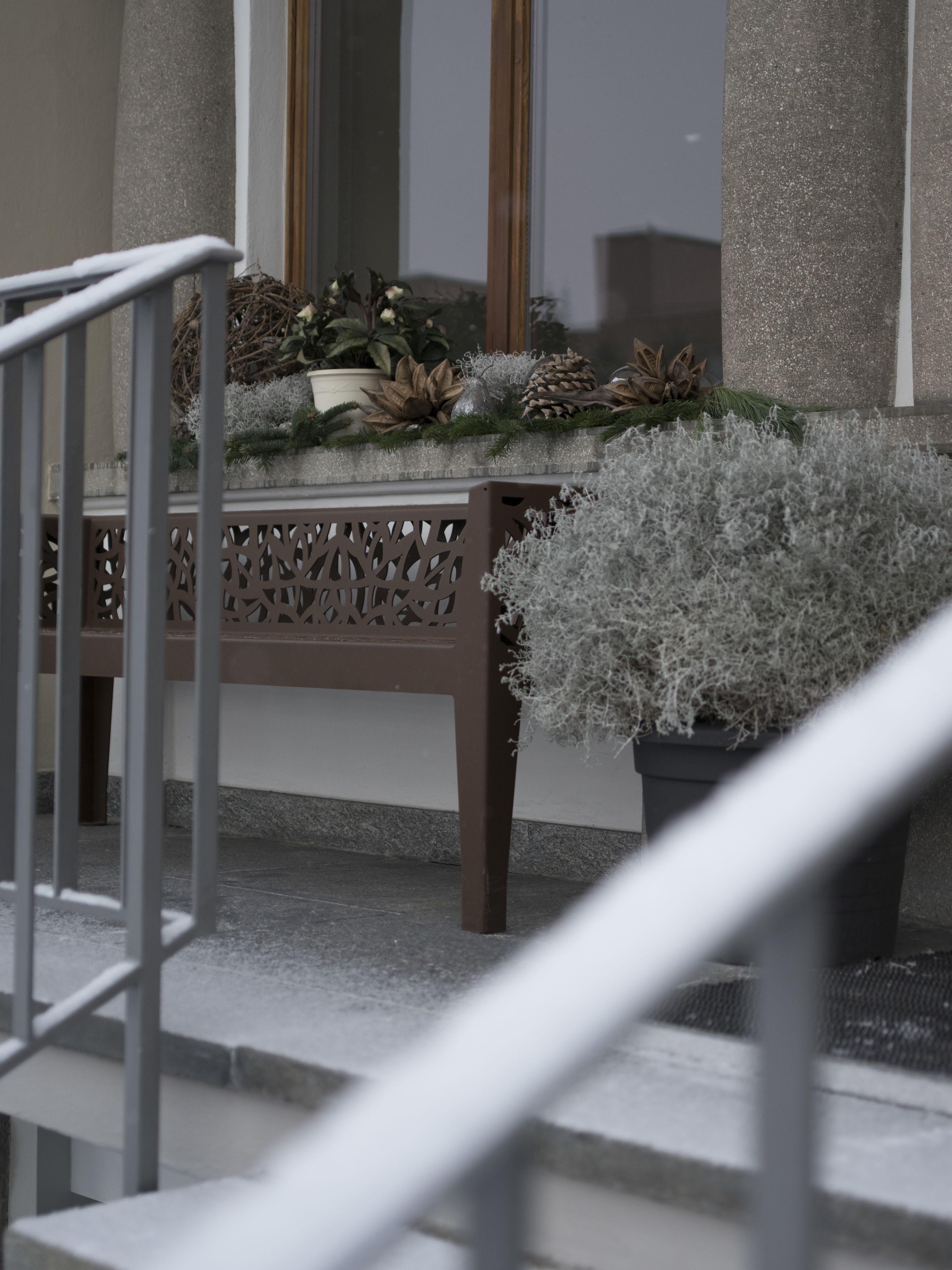 Una escalera con barandilla, un banco con un arreglo decorativo y una planta en maceta.