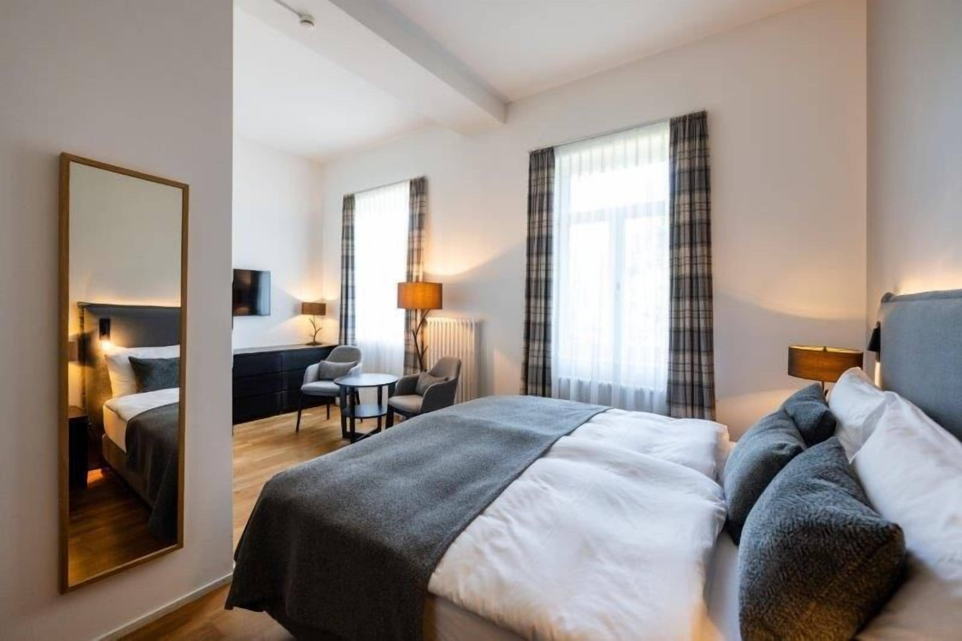A hotel room with a large bed, a desk, a chair, and a mirror.