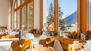 Un espace repas avec des chaises et des tables en bois, de grandes fenêtres offrant une vue sur les montagnes et un plafond en bois.