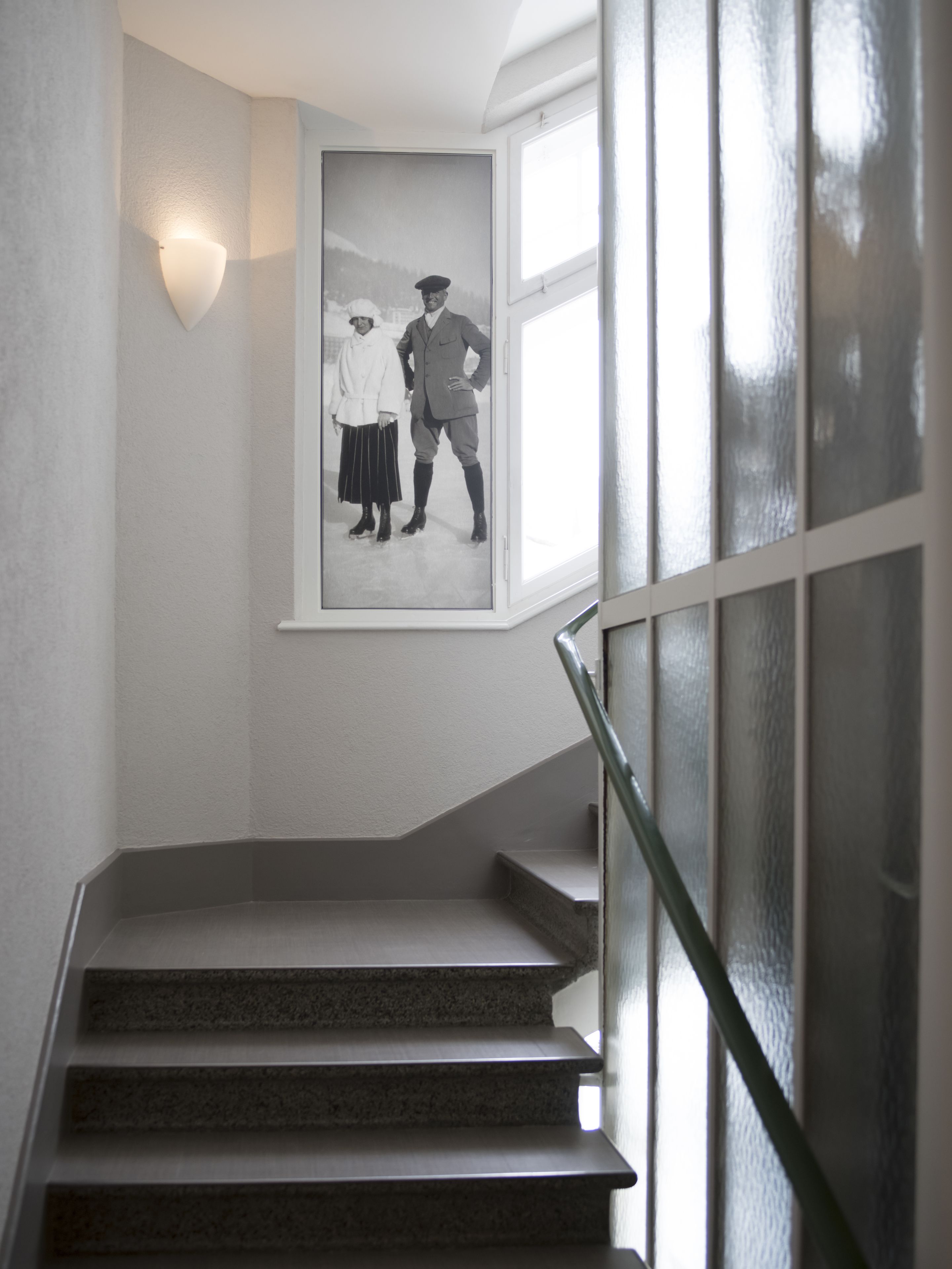 A staircase with a handrail, a wall-mounted light, and a framed black and white photograph.