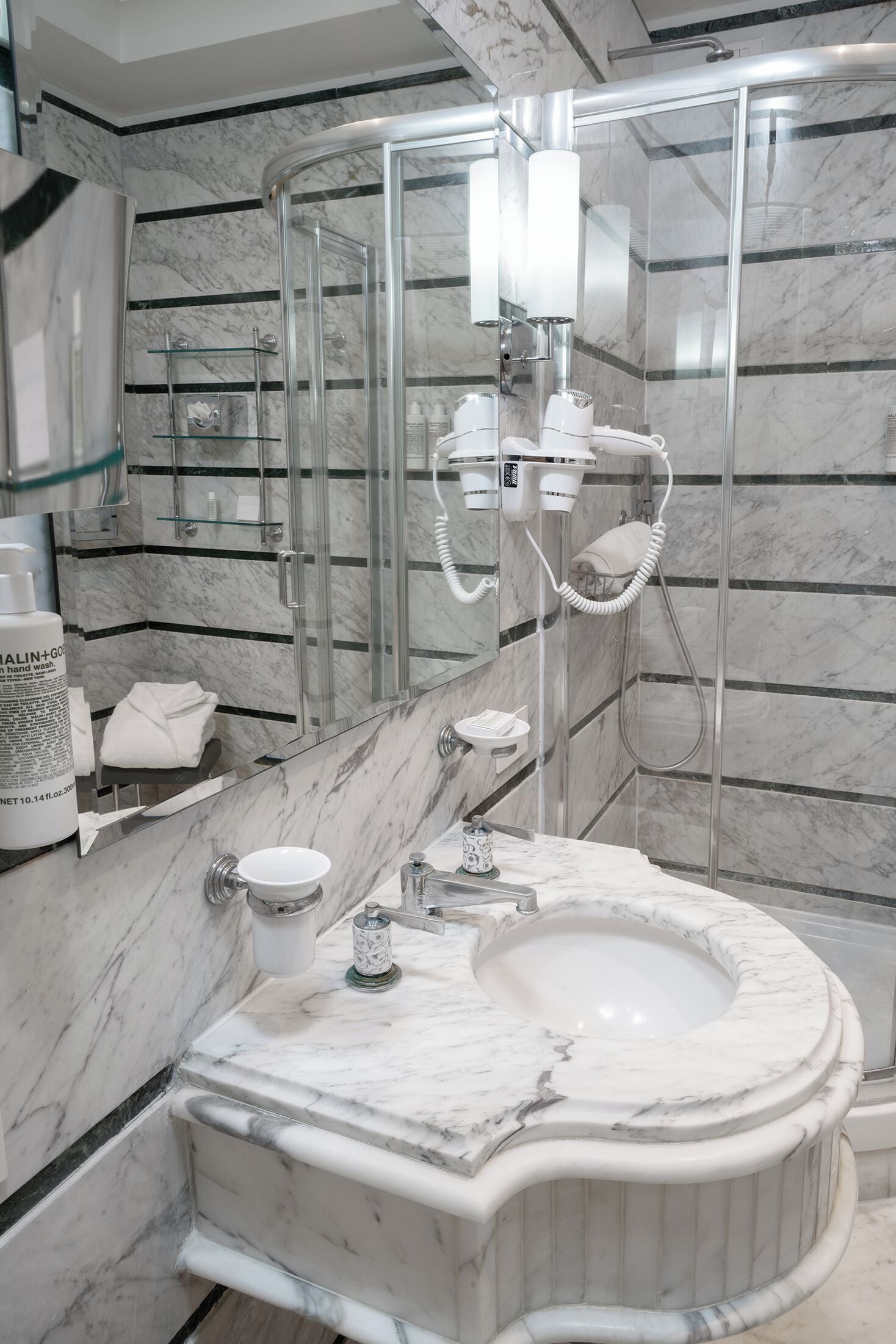 Une salle de bain moderne avec un lavabo en marbre, une cabine de douche en verre et un porte-serviettes.