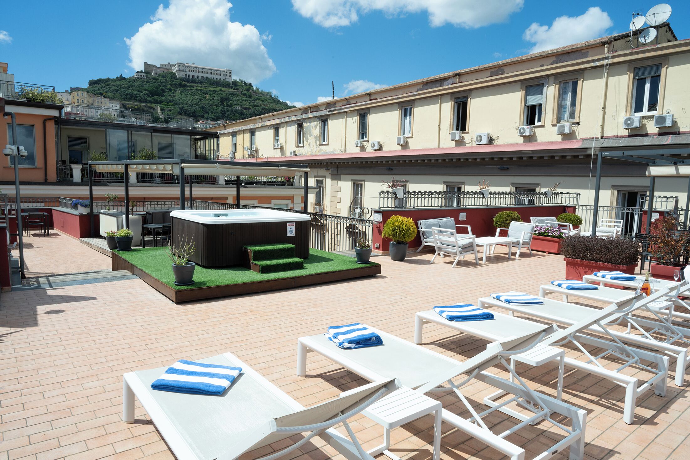 A rooftop terrace with lounge chairs, a hot tub, and potted plants.