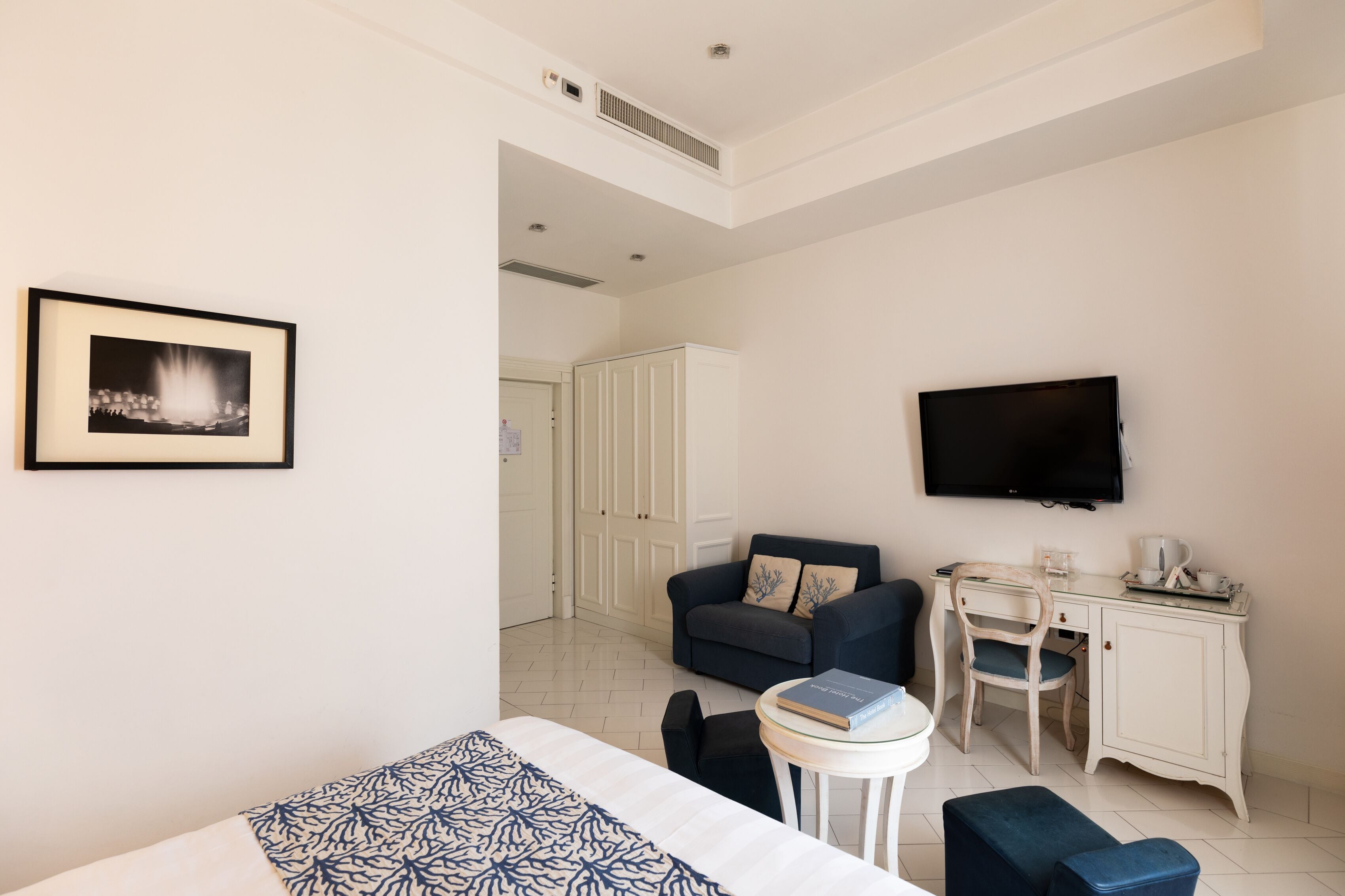 A hotel room with a bed, a desk with a chair, a television, and a framed picture on the wall.