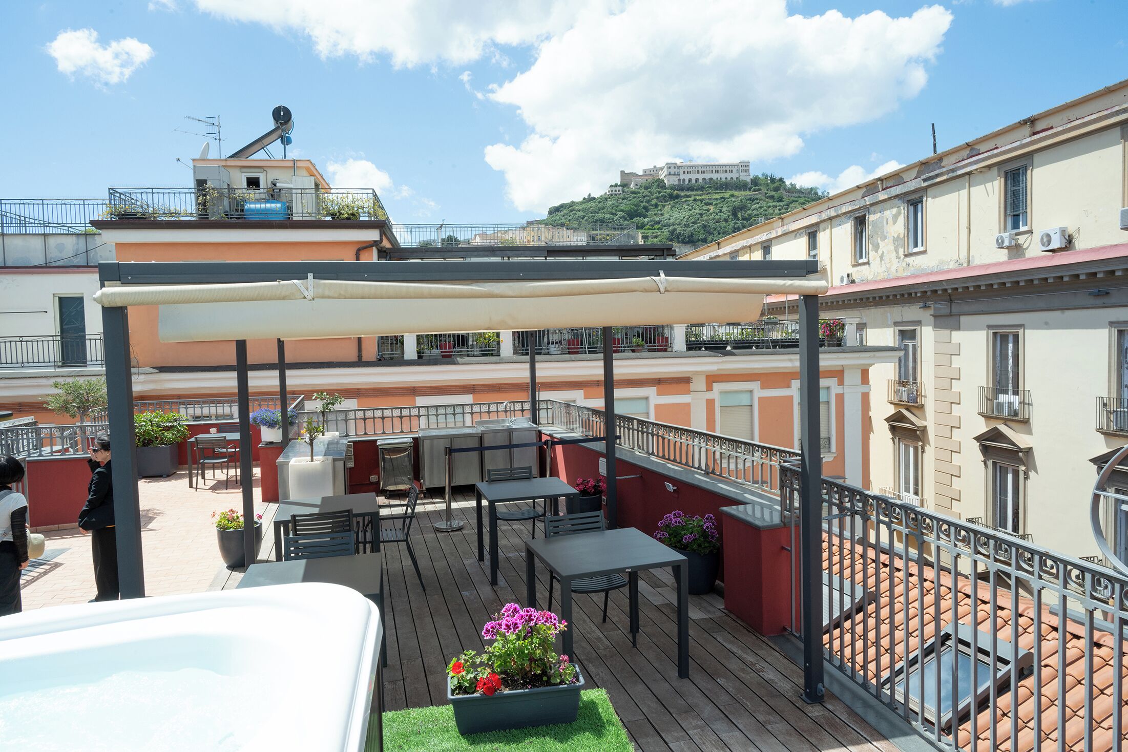 Una terraza en la azotea con mobiliario exterior, una pérgola y vistas a un edificio en la colina.