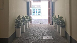A hallway with a cobblestone floor, white walls, and a large arched doorway leading to a bright room.