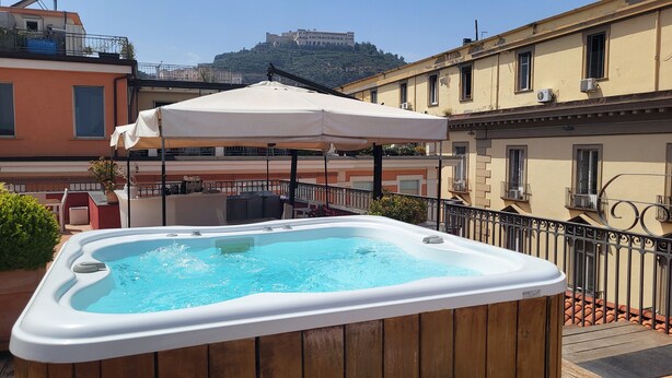 A hot tub on a balcony with a view of a hill and a historic building.