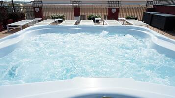 Een bubbelbad met een Jacuzzi logo, omringd door ligstoelen en potplanten.