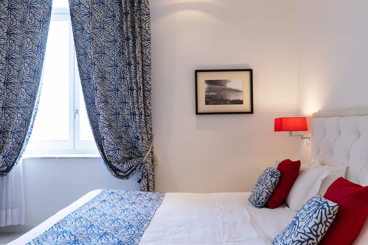 Habitación de hotel con cama, un cuadro en la pared y una ventana con cortinas.