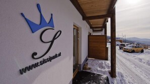 A hotel entrance with a crown logo, a website URL, and a view of a snowy landscape with parked cars. - Sissi Park (Oberwölz)