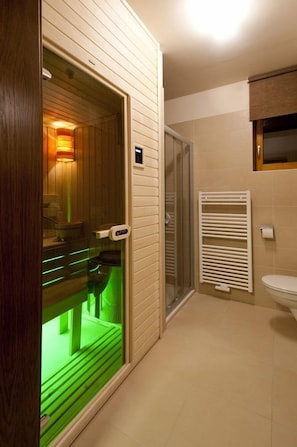 Un baño moderno con sauna, puerta de vidrio, inodoro blanco y toallero.