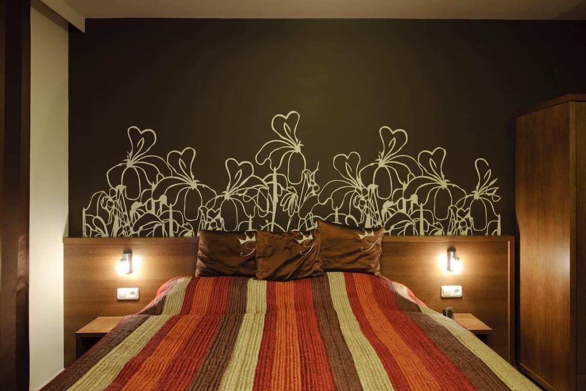 Una cama con un edredón a rayas, dos lámparas de noche y una pared con un estampado floral blanco.