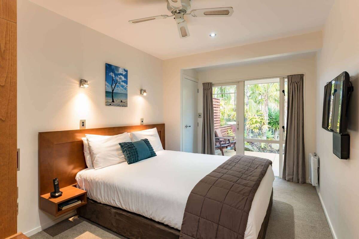 Une chambre d’hôtel avec un grand lit, un ventilateur de plafond, un téléviseur fixé au mur et une vue sur l’extérieur grâce à une porte-fenêtre coulissante.