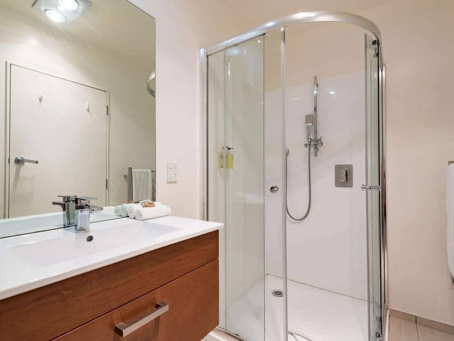 A modern bathroom with a glass-enclosed shower, a white vanity with a mirror, and a wooden cabinet.