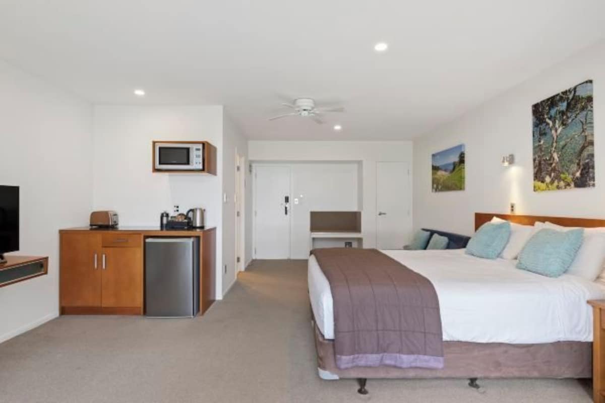 A hotel room with a bed, a desk with a computer, a microwave, and a refrigerator.